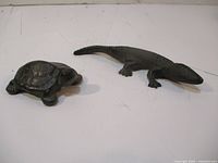 Photo showing cast iron turtle and lizard laid side by side on a light surface, highlighting size and texture of each figurine.