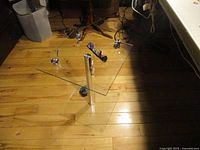 Full view of glass and chrome end table showing triangular glass top, chrome support column, and triangular glass base on wooden floor.