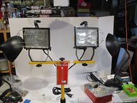 Dual square halogen lamps with wire guards and supporting frame, mounted on adjustable yellow tripod stand, viewed from the front.