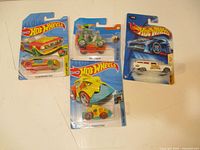 Four Hot Wheels cars in original packaging shown from an overhead view on a flat surface.