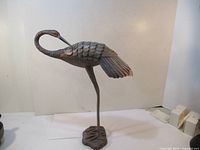 Full side view photo of the metal bird sculpture showing the curved neck, detailed feather texture, and round base.