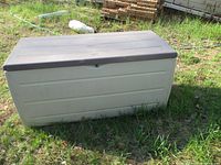Angle view of storage box showing beige body with horizontal panel details and dark gray lid closed.