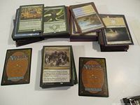 Stacks of Magic: The Gathering cards in protective sleeves arranged on a white surface showing backs and some faces of the cards