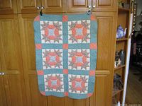 Full view of the patchwork quilt hanging, showing the overall pattern, colors, and size in relation to a cabinet behind it.
