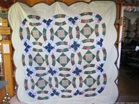 Full view of quilt showing double wedding ring pattern in green, blue, taupe, and floral fabrics on cream background with scalloped edges.