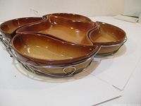 Photo showing side angle of 6 brown ceramic serving trays in metal holder, demonstrating shape and color.