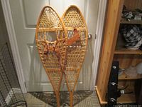 Pair of wooden frame snowshoes with woven rawhide, standing upright indoors against a white door.