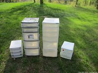 Four plastic storage drawer units of varying sizes arranged on grass outside, showing front and side views.