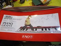 Red and white box for The Big Piano by FAO Schwarz with image of child playing on large piano mat