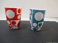 Two art cups, one red design and one blue design, side by side showing full front view.