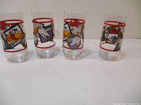Four Coca-Cola glasses with colorful cartoon artwork and red rings