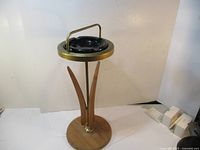 Front and angled view showing wooden base, brass frame and handle, and black ashtray insert