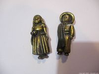 Front view of two brass brooches shaped as figurines of a woman and a man in traditional clothing, approximately 2 inches tall.