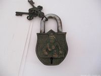 Vintage brass Krishna padlock showing front with seated Krishna figure in relief and attached to a ring holding two antique-style keys.