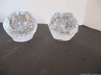Two textured crystal candle holders shaped like snowballs, sitting side-by-side on a black surface.