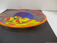 Side angled view of the glass centerpiece bowl showing orange rim, yellow and red internal glass accents with blue and red abstract swirls.