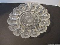 Top down view showing full 11 inch vintage clear glass deviled egg plate with decorative pressed glass patterns and 12 scalloped egg slots.