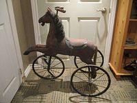 Side view of the vintage wooden horse ride-on toy showing the detailed carving, metal wheels, and overall structure.