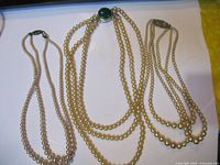 Three pieces of faux pearl jewelry laid out including two necklaces and one bracelet with decorative clasps.