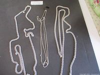 Three silver-tone chain link necklaces laid out on dark background, showing length and style differences.