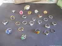 Photo showing 23 vintage rings of different styles including floral, gemstone, and plain bands arranged on a black surface.