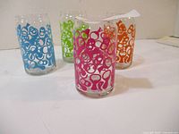 Four colorful vintage pull top glasses in blue, green, pink, and orange with abstract patterns
