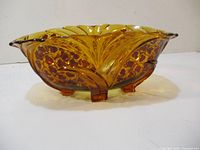 Side angle view showing amber glass, red decorative pattern, and molded feet of the bowl.