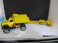 Two vintage Tonka trucks side-by-side showing relative size and condition, including yellow dump truck and toy trailer truck with connecting hitch.