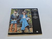 Front cover of ABBA Greatest Hits vinyl record showing two members outdoors on a bench with autumn setting.