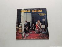 Front cover of Creedence Clearwater Revival album Cosmo's Factory showing band members in a room, one on a bicycle.