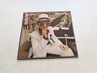 Front of the album cover showing Elton John in white suit and hat sitting at a piano.