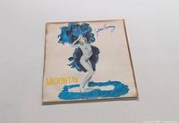Front cover of the "Moontan" album by Golden Earring showing a woman in a blue feathered costume.