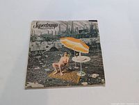 Front cover of Supertramp vinyl record Crisis? What Crisis? showing man in shorts under umbrella in an industrial scene.