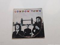 Front cover of Wings 'London Town' LP showing three band members and Tower Bridge in London, with colorful title text.