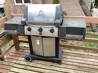Front view of Broil King propane BBQ grill showing stainless steel door, control knobs, and side shelves with dust and wear.