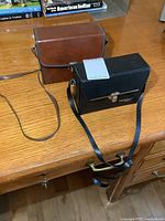 Two binocular cases on a wooden desk, one black with strap and one brown leather-like with strap.