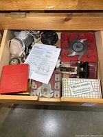 Top view of the wooden drawer containing various woodworking tools including red cases, a large molding cutter blade, a white plastic circle cutter case, and a box labeled Micro-mesh.