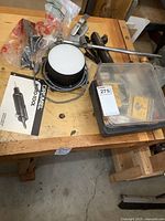 Photo showing the Dremel rotary tool stand, accessory box with blades, and tool case with manual on a wooden workbench.