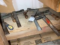 Overview of five heavy duty F clamps with wooden handles on wooden shelf, showing size variety and condition