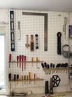 Wide view of pegboard with various mounted hand tools including levels, measuring squares, screwdrivers, and nut drivers