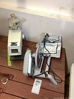 Photo of Rival electric food slicer and Grind O Matic meat grinder on wooden surface, showing both appliances with power cords and plug details.