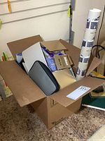 Open cardboard box showing manuals, boxes, zippered case and rolled poster