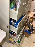 Photo of file cabinet drawers filled with office supplies including folders, notebooks, and assorted paper items.
