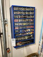 Front view of blue metal organizer with clear plastic drawers and assorted hardware inside.