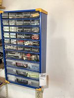 Front and side view of a blue metal wall-mounted organizer cabinet with 28 transparent plastic drawers filled with various small hardware items and accessories.