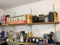 Photo showing two shelves with multiple cans and jars of wood stains, varnishes, some paint jars, and a box of preserving jars.