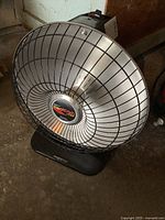 Front and angled view of Presto HeatDish parabolic electric heater showing metal heat reflector and plastic base.