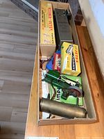Box containing vintage steam engine model parts including brass cylinder, green metal base with gear and crank wheel, and boxed Jetex accessories.