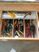 Drawer open showing compartments with pliers, wire cutters, screwdrivers, and measuring rulers including protractor.