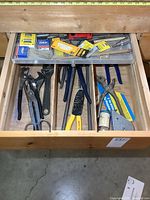 Wooden drawer containing multiple hand tools organized in compartments, including different types of pliers, cutters, and wrench.